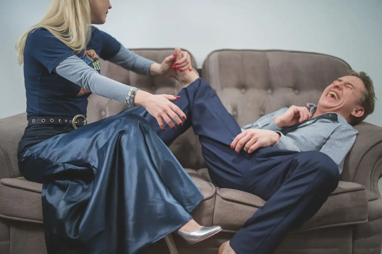 Blonde-Woman-Gripping-Husbands-Leg-While-Laughing-on-Sofa